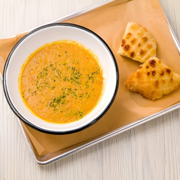 A bowl of creamy orange soup with herbs and two pieces of baked bread on a tray.